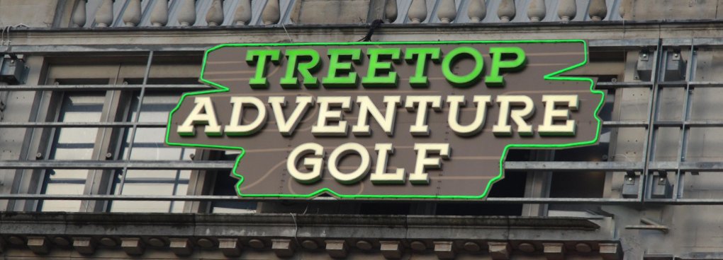 Daytime view of the Treetop Adventure Golf signage displayed on the exterior facade of Manchester Printworks