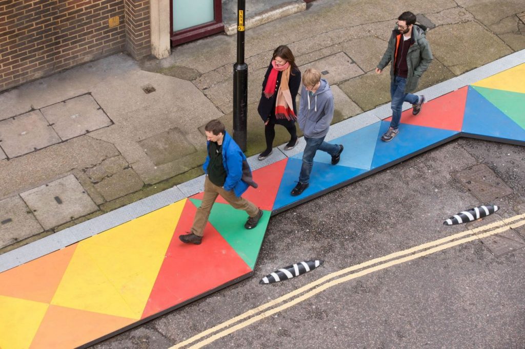 Aerial view of people walking along a multi-coloured geometric designed 'boardwalk' in an urban setting