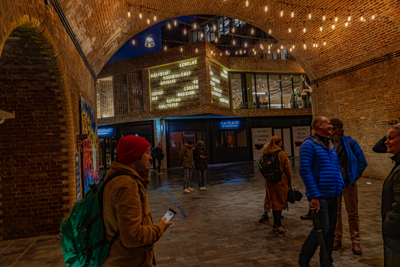 Tour attendees standing beneath fairy lights strewn across a pathway in Borough Yards development